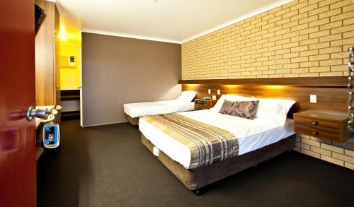 een hotelkamer met 2 bedden en een bakstenen muur bij Sarina Motor Inn in Sarina