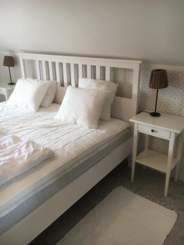 Bett mit weißer Bettwäsche und Kissen neben einem Tisch in der Unterkunft Jaktlyckan, Tuna Gård in Tuna