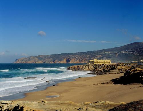 a beach with the ocean and mountains in the background at Grande Real Villa Itália Hotel & Spa in Cascais