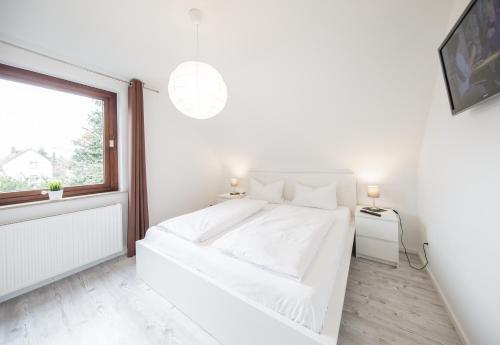 a white bedroom with a white bed and a window at Dünenhaus Steinmarne in Cuxhaven