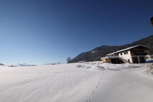 a snow covered field with a building in the background at Pfandlhof in Walchsee