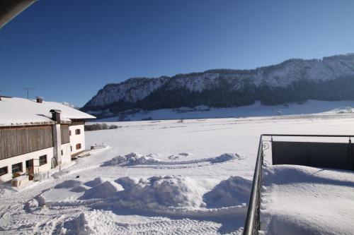 a snow covered yard next to a building with a pile of snow at Pfandlhof in Walchsee