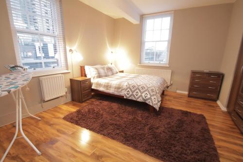 ein Schlafzimmer mit einem Bett, einer Kommode und zwei Fenstern in der Unterkunft Henley at Shoreditch in London