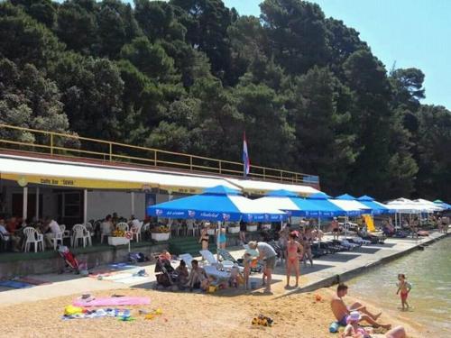 a group of people sitting on a beach with umbrellas at Riviera Rooms and Apartments in Rab