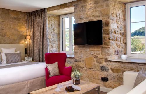 Habitación de hotel con cama y TV en una pared de piedra. en Domaine de la Klauss & Spa, Restaurant Gastronomique Le K, en Montenach