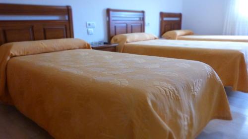 a room with three beds with orange sheets on them at Hostal Restaurante La Masía in Villareal