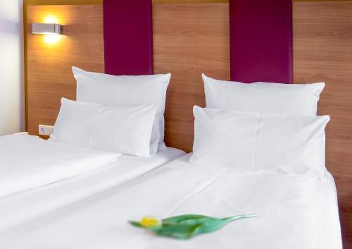 a green bird sitting on a bed with white pillows at TIPTOP Hotel Burgschmiet Garni in Nürnberg