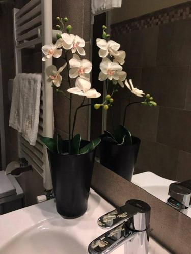 two black vases with white flowers on a bathroom sink at Villa Tivoli in Guidonia
