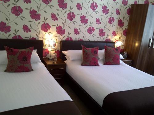 two beds in a room with pink flowers on the wall at Senlac Guesthouse in Hastings