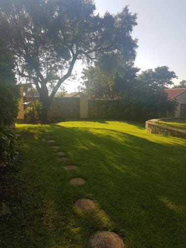 a grassy yard with a tree and a stone path at LightStone Guesthouse in Centurion