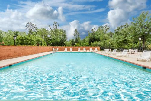 a large swimming pool with white chairs and a brick wall at Days Inn by Wyndham Williamsburg Historic Area in Williamsburg