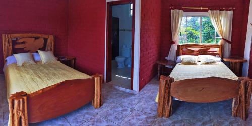 two beds in a room with a red wall at Hosteria Don Elias in Puyo