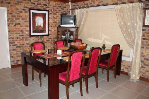 a dining room with a wooden table and red chairs at Quest Bed And Breakfast in Melkbosstrand