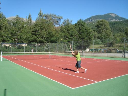 une personne frappant un ballon de tennis sur un court de tennis dans l'établissement Camping Les Grillons, à Embrun