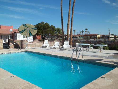 a swimming pool with chairs and a table and an umbrella at Hacienda Motel in Yuma