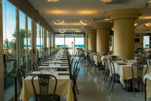 una sala da pranzo con tavoli e sedie con vista sull'oceano sullo sfondo di Hotel Miramare a Gabicce Mare