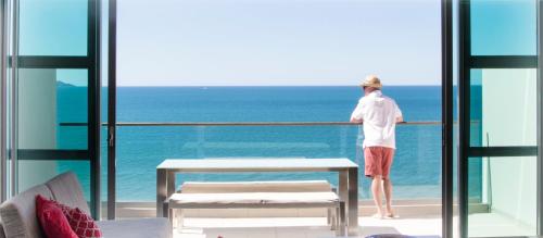 a man standing on a balcony looking out at the ocean at Doubtless Bay Villas in Cable Bay