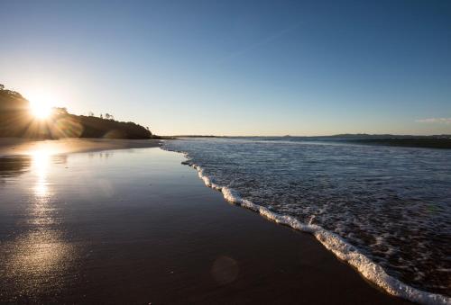 a beach with the sun rising over the water at Doubtless Bay Villas in Cable Bay