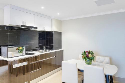 a kitchen with white cabinets and a table and chairs at Hotel Diana Woolloongabba in Brisbane