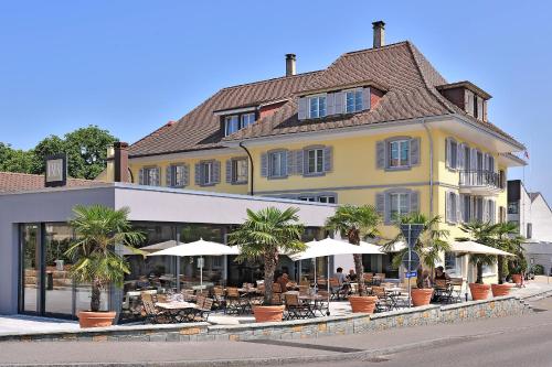 un bâtiment jaune avec des tables et des parasols dans une rue dans l'établissement Hotel Murten, à Morat