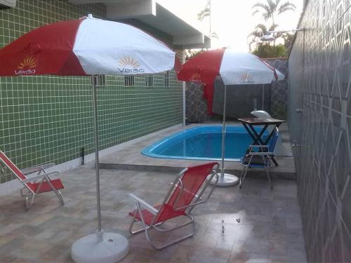 two umbrellas and chairs next to a swimming pool at Pousada raios de sol indaia in Bertioga