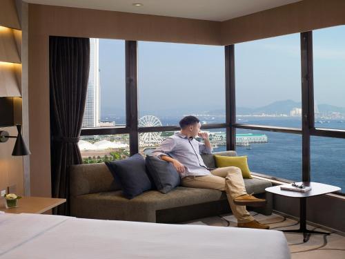 un hombre sentado en un sofá en una habitación de hotel en The Harbourview - Chinese YMCA of Hong Kong, en Hong Kong