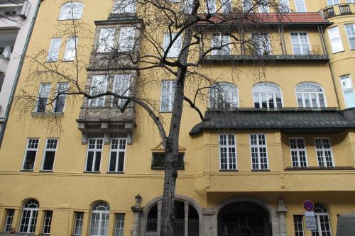 a yellow building with a tree in front of it at Hotel Pension Waizenegger am Kurfürstendamm in Berlin