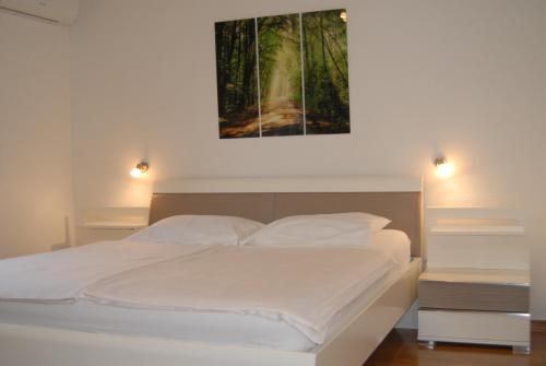 a bedroom with a white bed with a painting on the wall at Apartments Karabaic in Punat