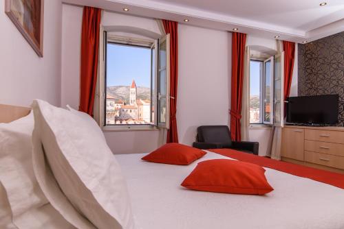 a bedroom with a bed with red pillows and a window at Heritage Hotel Vila Sikaa in Trogir