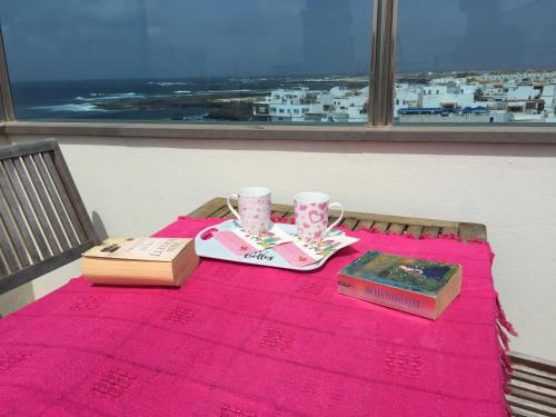 una mesa con un mantel rosa y dos tazas y un libro en Piso Oliastur, en Cotillo