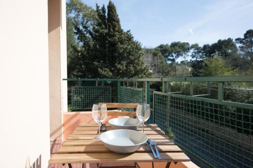 une table en bois avec deux bols et des verres à vin sur un balcon dans l'établissement Résidence La Source, à Toulon