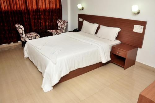 a bedroom with a large white bed and a chair at Emporium Hotel in Mangalore