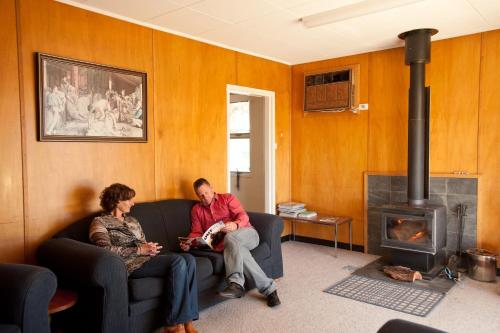 two people sitting on a couch in a living room with a fireplace at Black Jack Get-A-Way "Magpies Nest" in Orroroo