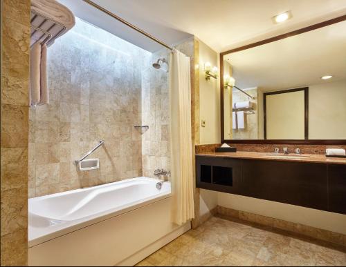 uma casa de banho com uma banheira, um lavatório e um espelho. em Aryaduta Lippo Village em Tangerang
