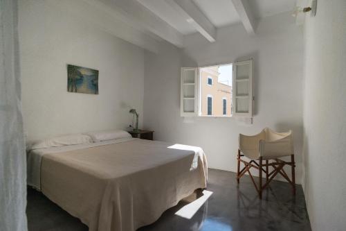 a white bedroom with a bed and a window at Curniola in Ciutadella