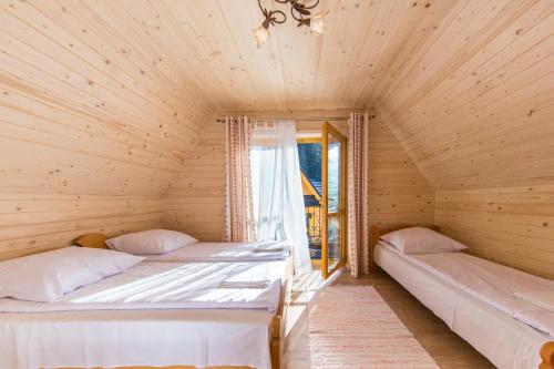 two beds in a wooden room with a window at Góralskie Zacisze Domki in Suche
