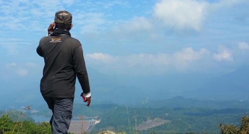 a man standing on top of a hill flying a kite at Ahaspokuna by Eco Team in Belihul Oya