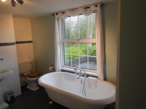 La salle de bains est pourvue d'une baignoire, d'une fenêtre et de toilettes. dans l'établissement Wishing Well Cottage, à Wilmington