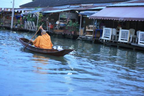Ein Mann in einem orangefarbenen Gewand paddelt ein Boot im Wasser. in der Unterkunft Ban Mae Arom in Amphawa