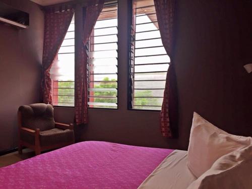 um quarto com uma cama, uma cadeira e janelas em Kokodo Guest House em Cape Coast