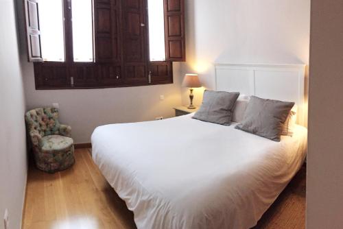 a bedroom with a white bed and a chair at 19th Century Sevillian Apartment in Seville