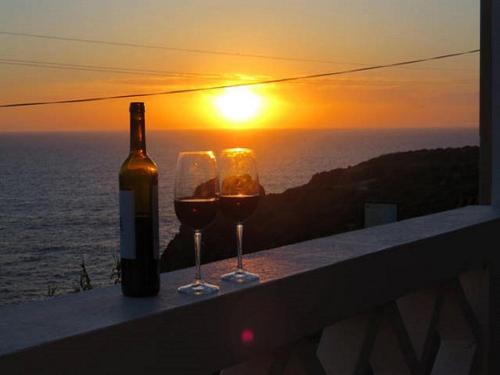 a bottle of wine and two glasses on a ledge with the sunset at Casas do Zé Zambujeira do Mar in Zambujeira do Mar