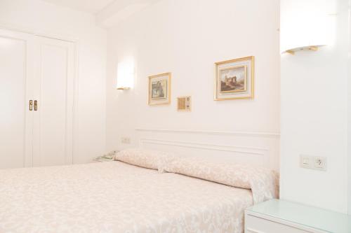 a white bedroom with a bed and two pictures on the wall at Rey Fernando in Santiago de Compostela