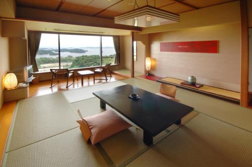a room with a table and chairs and a large window at Hotel Matsushima Taikanso in Matsushima