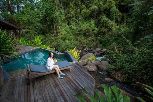 a woman sitting on a bench next to a swimming pool at Namkat Yorla Pa Resort in Ban Kat