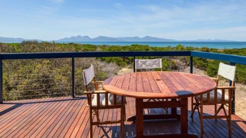 a wooden table and chairs on a deck with the ocean at Dolphin Beach House in Swansea