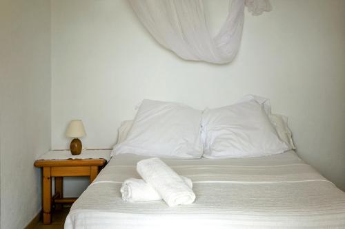 ein Bett mit weißen Kissen und einem Tisch mit einer Lampe in der Unterkunft Apartamentos Es Carnatge - Formentera Vacaciones in Playa Migjorn