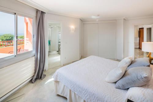 a white bedroom with a bed and a large window at La Reserva de Marbella Penthouse in Marbella