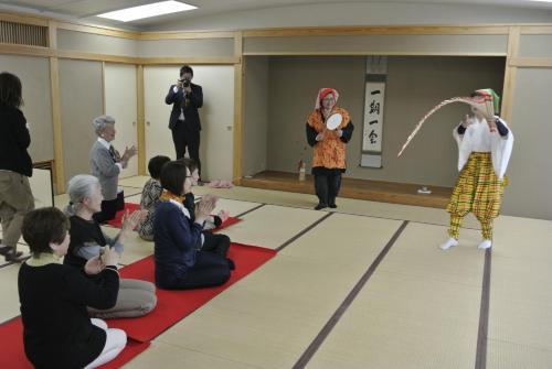 a group of people sitting on the floor watching two women performing dances at Daichan Farm Guest House in Asahi-machi