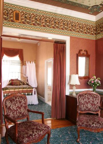 a bedroom with a bed and two chairs and a mirror at The Queen Victoria in Cape May